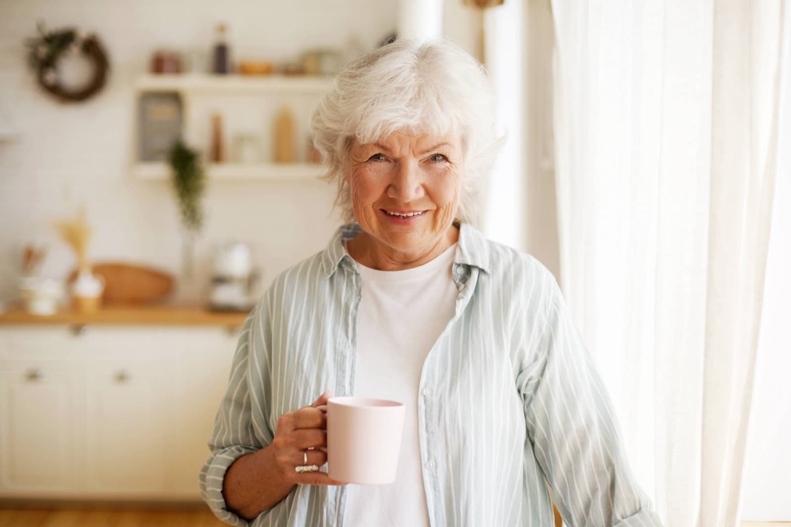 Lächelnde Seniorin mit einer Tasse Tee in ihrer Küche