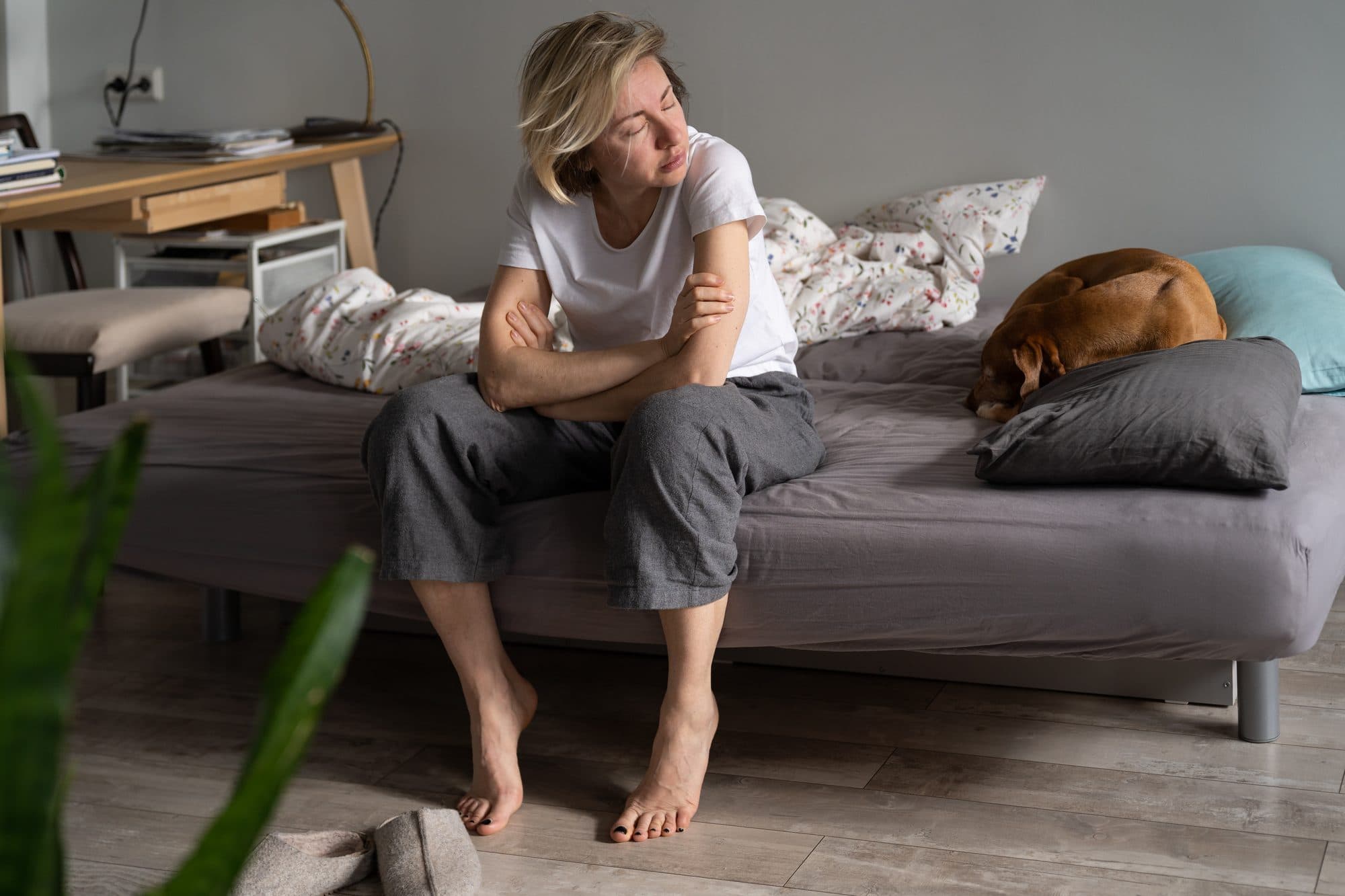 Erschöpfte pflegende Angehörige sitzt am Morgen müde auf der Bettkante – Warnsignale von Überlastung ernst nehmen und rechtzeitig Entlastung suchen
