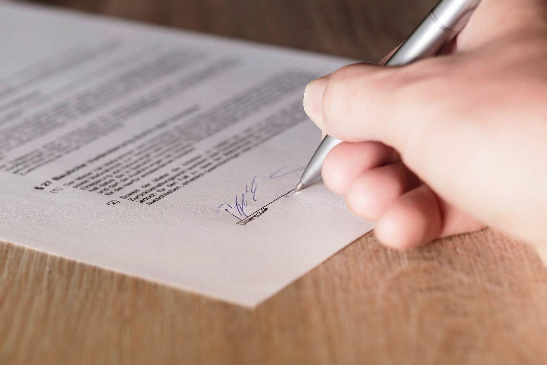 Hand unterschreibt mit einem Stift ein Dokument auf der Unterschrift-Zeile – Petition gegen die Kürzungen der Pflegereform 2026